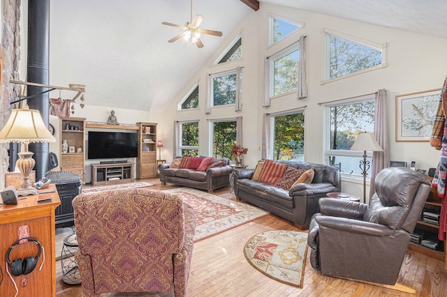 living room featuring wood-type flooring, a wood stove, ceiling fan, beam ceiling, and high vaulted ceiling