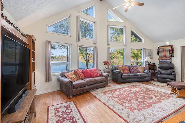 living room with ceiling fan, high vaulted ceiling, a textured ceiling, and hardwood / wood-style floors