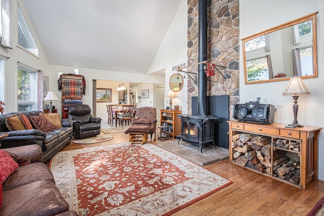 living room featuring high vaulted ceiling, a wood stove, and light hardwood / wood-style flooring