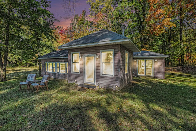 back house at dusk featuring a lawn