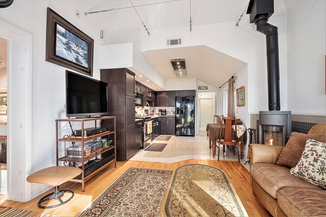 living room with a wood stove, high vaulted ceiling, and light wood-type flooring