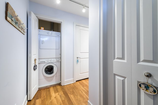 laundry room with light hardwood / wood-style flooring, stacked washing maching and dryer, and rail lighting