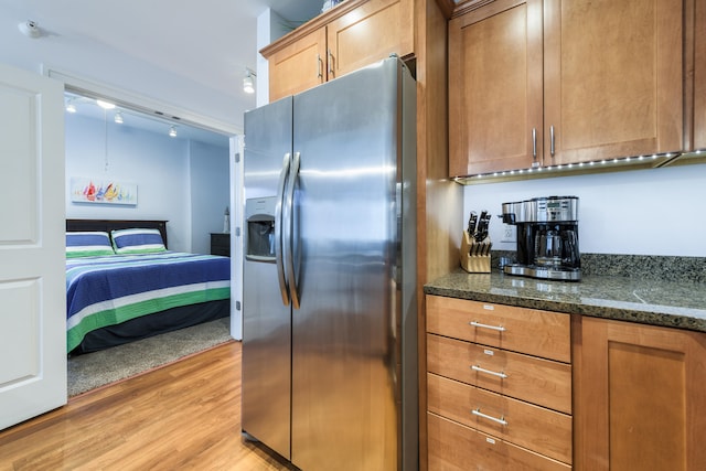 kitchen featuring stainless steel fridge, light hardwood / wood-style floors, and dark stone countertops