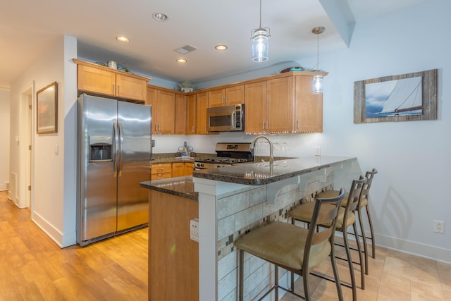 kitchen featuring kitchen peninsula, hanging light fixtures, light hardwood / wood-style flooring, dark stone countertops, and stainless steel appliances