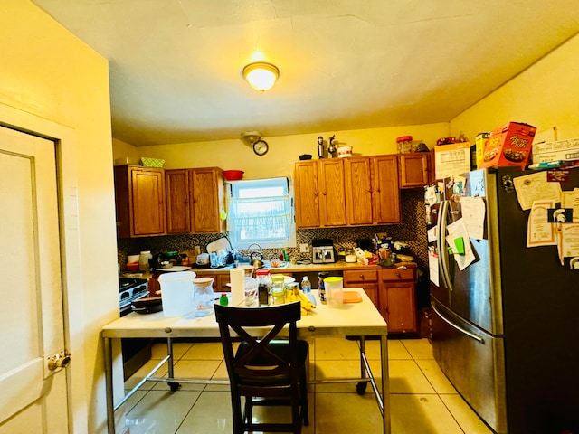 kitchen with sink, backsplash, a breakfast bar area, stainless steel refrigerator, and light tile patterned floors