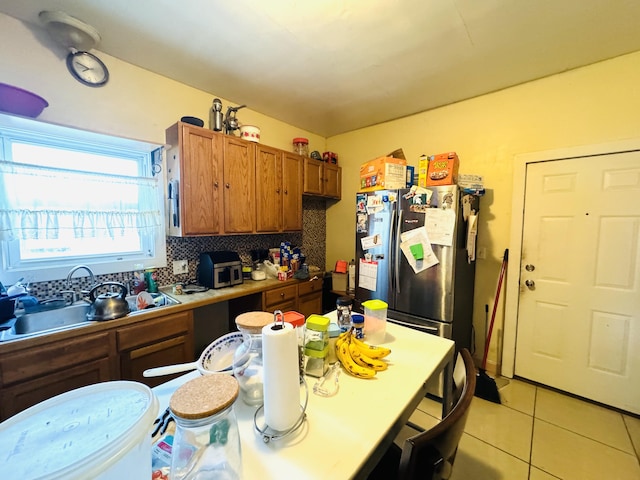 kitchen featuring backsplash, sink, light tile patterned floors, and stainless steel fridge