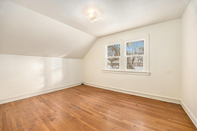 additional living space with a textured ceiling, hardwood / wood-style floors, and vaulted ceiling