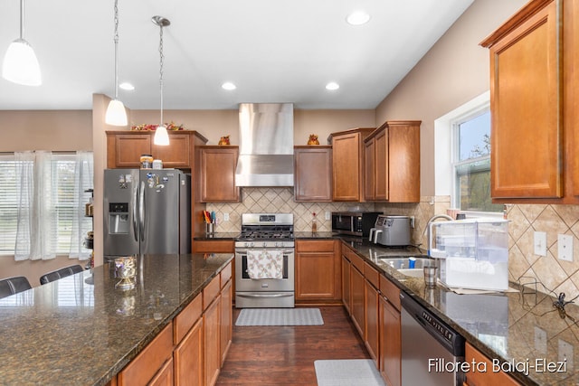 kitchen featuring tasteful backsplash, stainless steel appliances, wall chimney exhaust hood, decorative light fixtures, and dark wood-type flooring