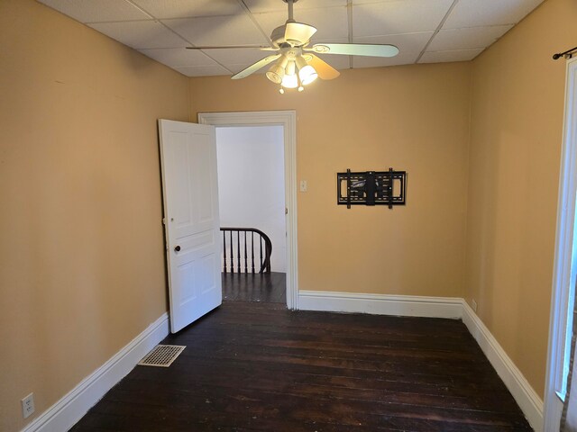 empty room with a drop ceiling, ceiling fan, and dark hardwood / wood-style flooring