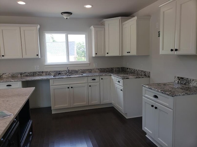 kitchen with white cabinets, dark hardwood / wood-style flooring, light stone counters, and sink