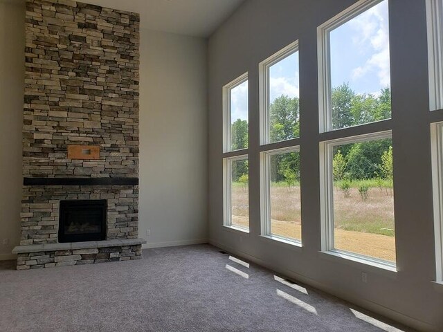 unfurnished living room with carpet, a stone fireplace, and a high ceiling