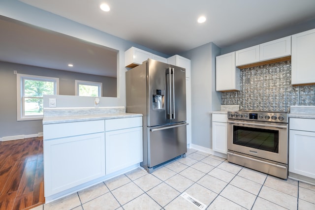 kitchen with light hardwood / wood-style floors, white cabinetry, stainless steel appliances, and backsplash