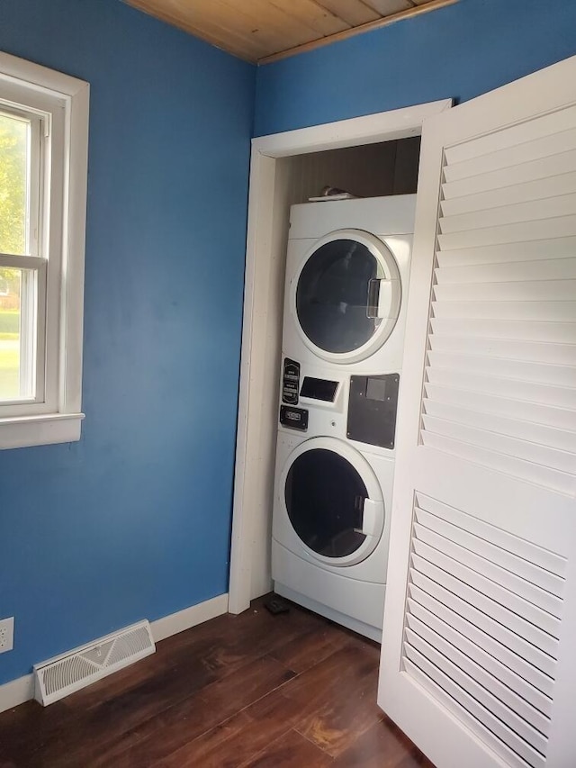 clothes washing area featuring stacked washing maching and dryer, dark hardwood / wood-style flooring, and wood ceiling