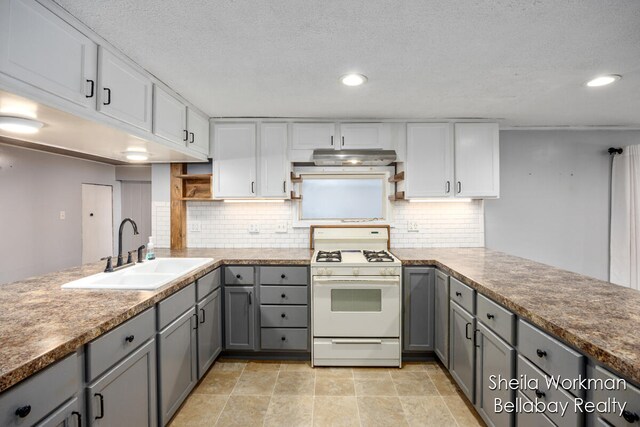 kitchen featuring sink, backsplash, white gas range oven, kitchen peninsula, and gray cabinets