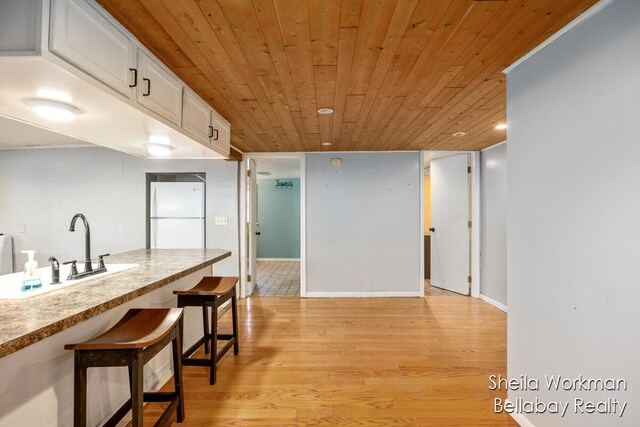 kitchen with wood ceiling, a breakfast bar area, light hardwood / wood-style flooring, white cabinetry, and white fridge