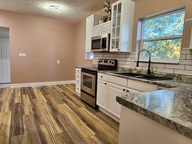 kitchen featuring white cabinets, backsplash, appliances with stainless steel finishes, a textured ceiling, and light wood-type flooring