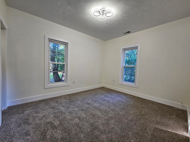 empty room with a textured ceiling, a healthy amount of sunlight, and dark carpet