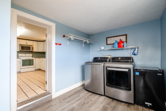 laundry area with a textured ceiling, separate washer and dryer, and light wood-type flooring