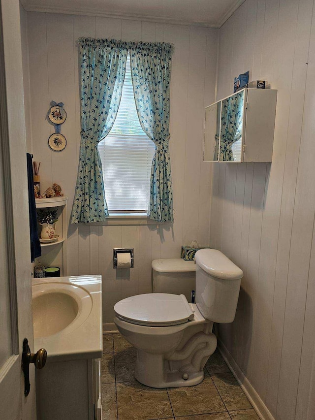 bathroom with toilet, ornamental molding, vanity, and wooden walls