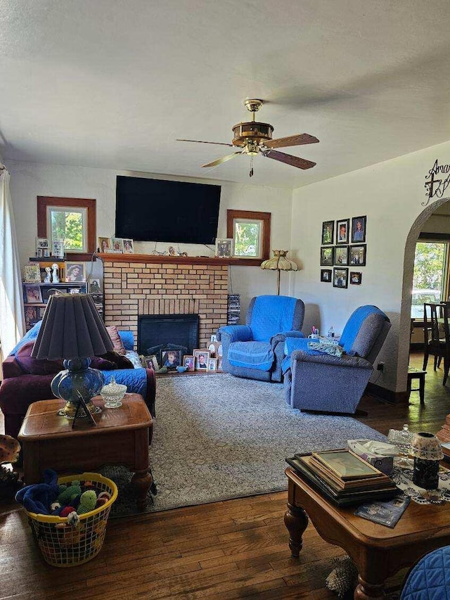 living room featuring ceiling fan, a wealth of natural light, a brick fireplace, and dark hardwood / wood-style floors