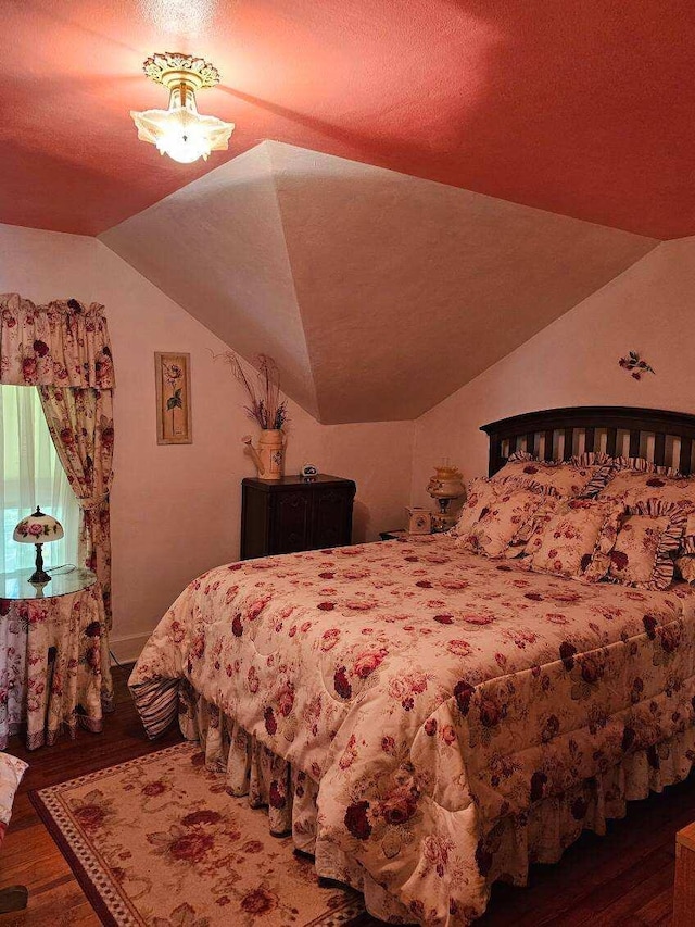 bedroom with dark wood-type flooring, a textured ceiling, and vaulted ceiling