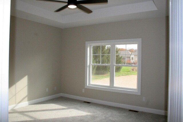 carpeted spare room featuring ceiling fan and a raised ceiling