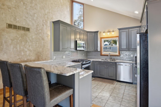 kitchen with gray cabinets, sink, appliances with stainless steel finishes, and a kitchen bar