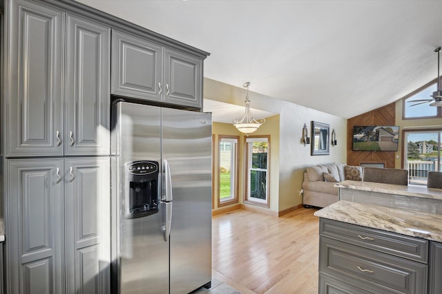 kitchen with lofted ceiling, hanging light fixtures, stainless steel fridge with ice dispenser, light stone counters, and light hardwood / wood-style floors