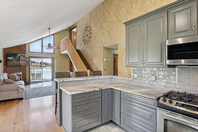 kitchen featuring kitchen peninsula, ceiling fan, high vaulted ceiling, light hardwood / wood-style floors, and stainless steel appliances