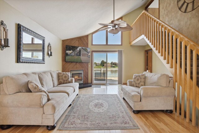 living room featuring light hardwood / wood-style flooring, wood walls, high vaulted ceiling, and ceiling fan