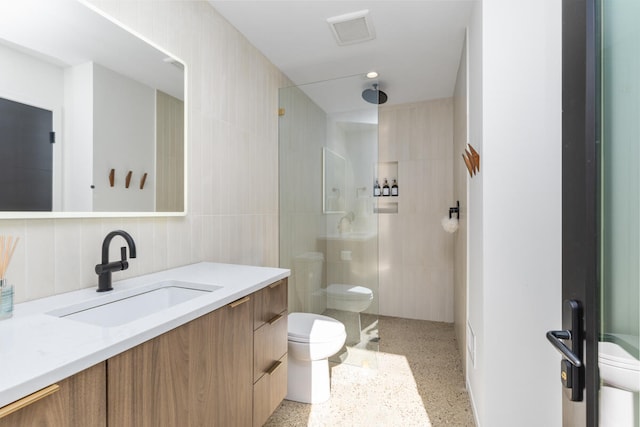 bathroom featuring vanity, toilet, tile walls, and a tile shower