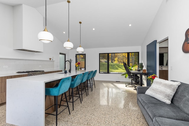 kitchen with lofted ceiling, an island with sink, sink, a kitchen bar, and pendant lighting