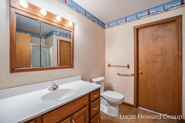 bathroom featuring hardwood / wood-style floors, a textured ceiling, toilet, vanity, and an enclosed shower