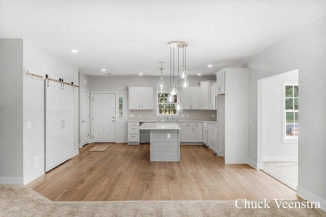 kitchen featuring tasteful backsplash, a barn door, a center island, white cabinetry, and hanging light fixtures