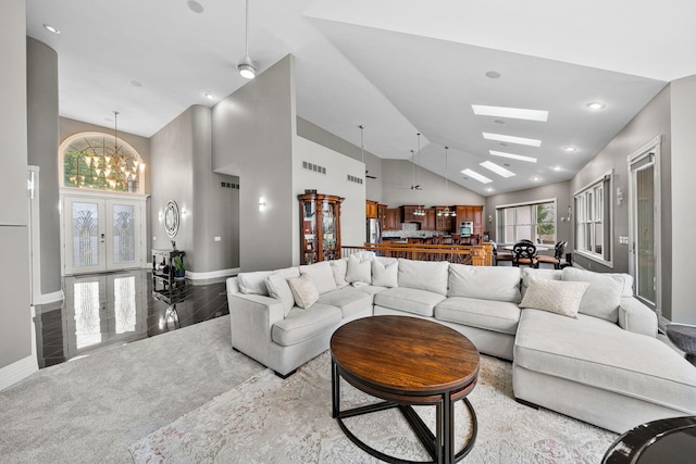 living room with an inviting chandelier, high vaulted ceiling, wood-type flooring, a skylight, and french doors