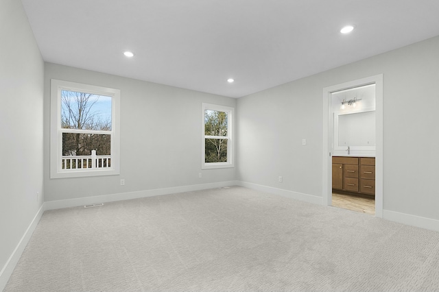 unfurnished bedroom featuring sink, light carpet, connected bathroom, and multiple windows