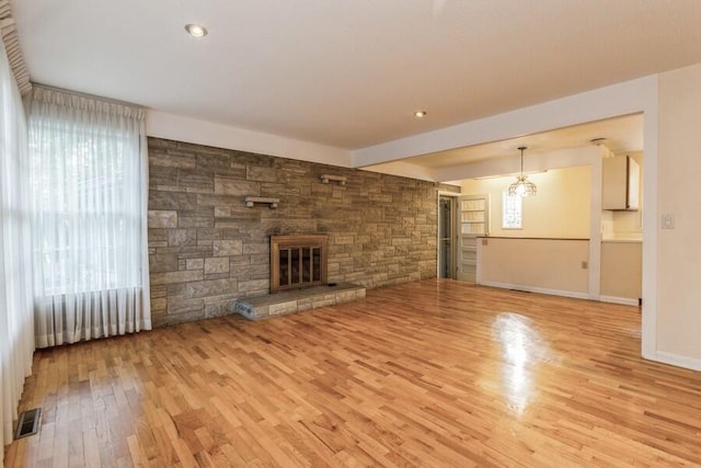 unfurnished living room featuring wood finished floors, visible vents, baseboards, and a stone fireplace