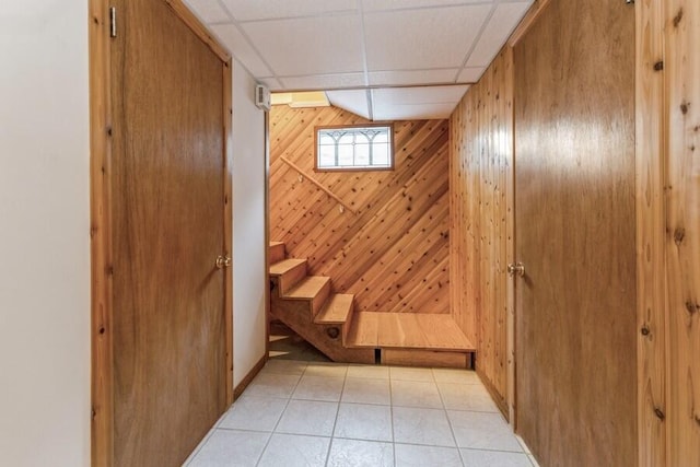 interior space featuring a drop ceiling, light tile patterned flooring, and wooden walls