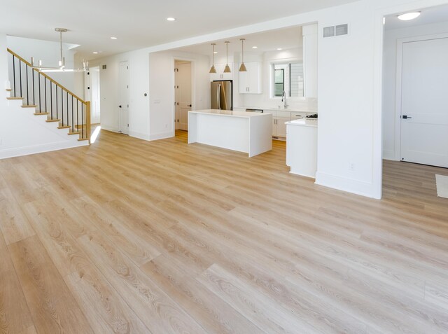 unfurnished living room with an inviting chandelier, light hardwood / wood-style flooring, and sink