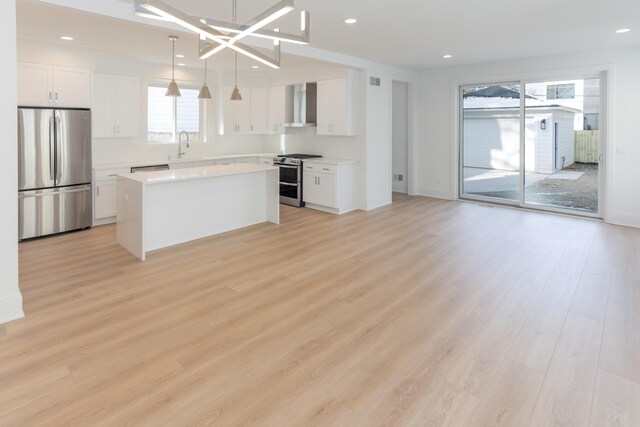 kitchen with appliances with stainless steel finishes, wall chimney range hood, decorative light fixtures, white cabinets, and a center island