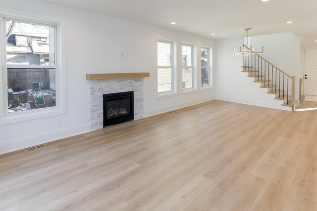 unfurnished living room with an inviting chandelier, light hardwood / wood-style flooring, and a stone fireplace