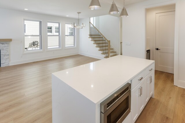 kitchen with white cabinets, light hardwood / wood-style flooring, built in microwave, decorative light fixtures, and a kitchen island