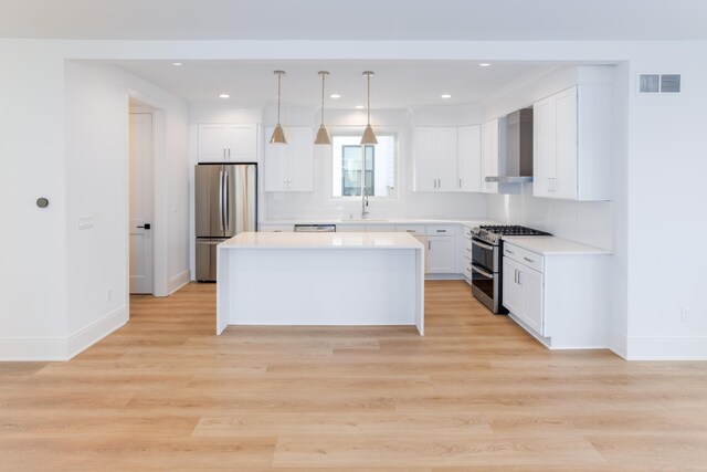 kitchen featuring sink, wall chimney exhaust hood, stainless steel appliances, pendant lighting, and white cabinets