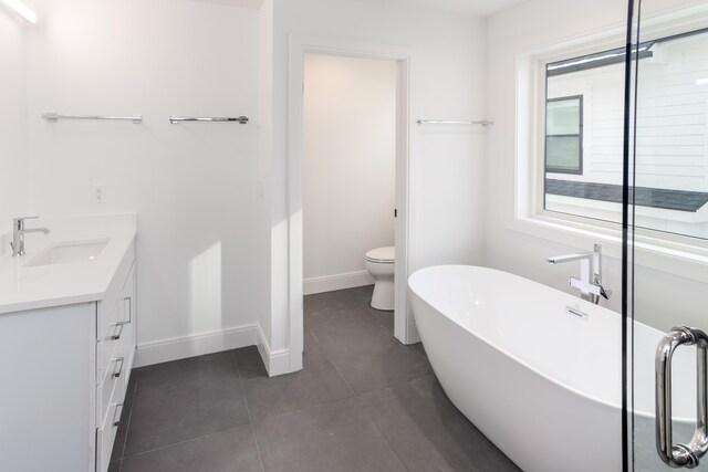 bathroom with tile patterned flooring, vanity, toilet, and a tub to relax in