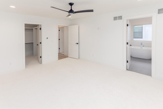 unfurnished bedroom featuring light carpet, ensuite bath, ceiling fan, a spacious closet, and a closet