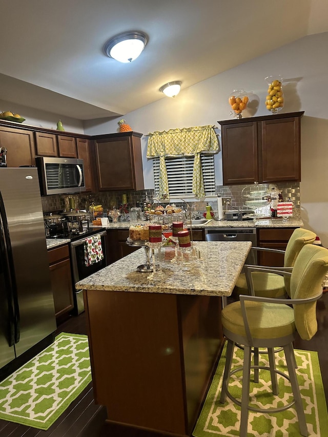 kitchen with dark brown cabinetry, light stone counters, a kitchen island, and appliances with stainless steel finishes