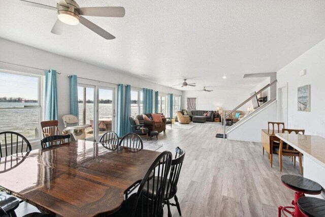 dining area with a water view, light hardwood / wood-style floors, and a textured ceiling