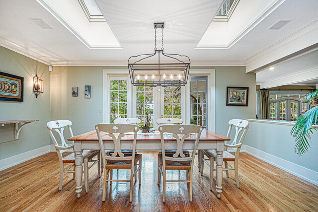 dining space with light hardwood / wood-style floors, crown molding, a notable chandelier, and a skylight