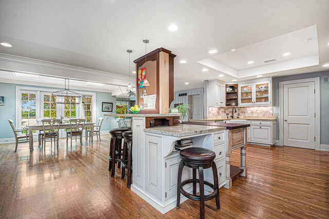 kitchen with a kitchen breakfast bar, hanging light fixtures, kitchen peninsula, white cabinetry, and dark hardwood / wood-style flooring