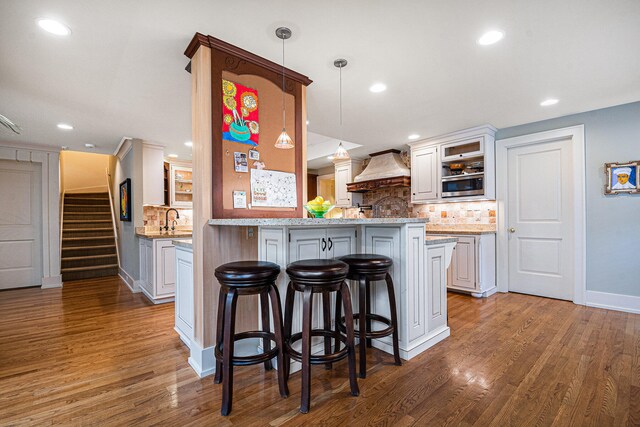 kitchen with a kitchen breakfast bar, kitchen peninsula, wood-type flooring, decorative light fixtures, and custom exhaust hood